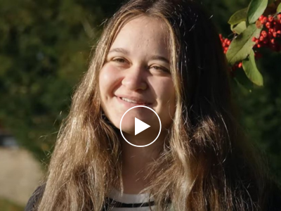 A student smiling in front of a hedge